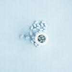 white-pills-with-open-plastic-bottle-blue-background